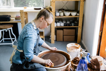 Side view of woman cleaning pottery wheel at workshop - CAVF20623