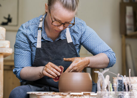 Woman working on pottery wheel in workshop - CAVF20629