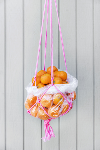 Strauß frischer Orangen in einem Seilkorb, der an einer Holzwand hängt, lizenzfreies Stockfoto