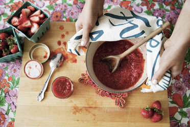 Overhead view of woman holding strawberry preserve in bowl on cutting board - CAVF20699