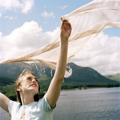 Schöne Frau hält Schal durch See und Berg gegen bewölkten Himmel - CAVF20738