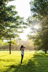 Young woman using retro styled camera while standing on grassy field - CAVF20778