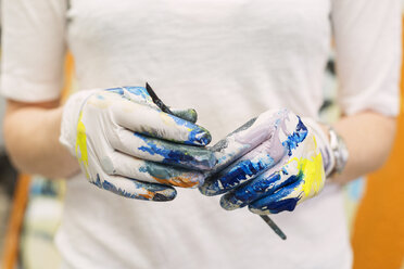 Nahaufnahme einer Künstlerin mit Handschuhen, die einen Pinsel im Kunstatelier hält - CAVF20815