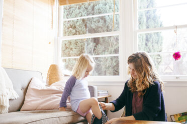 Mutter, die ihrer Tochter beim Anziehen hilft, am Fenster zu Hause - CAVF20838