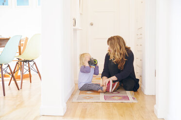 Mother helping playful daughter to wear shoe against door in passage - CAVF20839