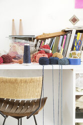 Various threads, yarns and books on table by chair against wall at home - CAVF20847