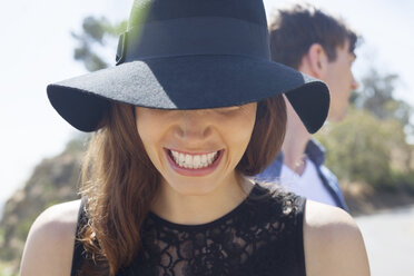 Nahaufnahme einer glücklichen Frau mit schwarzem Hut und einem männlichen Freund im Hintergrund - CAVF20861