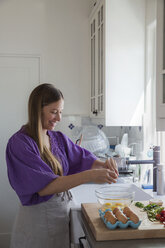 Glückliche Frau schlägt Eier in einer Rührschüssel auf, während sie in der Küche steht - CAVF20890