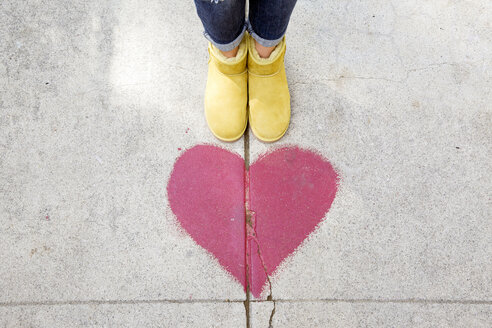 Low section of person standing by red heart shape on footpath - CAVF21014