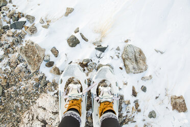 Low section of woman wearing snowshoes while standing on snow covered field - CAVF21016