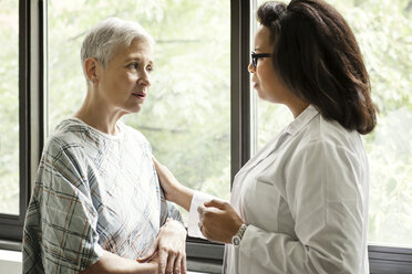 Doctor having discussion with patient while standing by window in hospital - CAVF21052