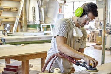 Schreiner mit Gehör- und Augenschutz beim Schleifen von Holzbrettern in der Werkstatt - CAVF21119
