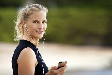 Porträt einer lächelnden Frau, die über ihr Smartphone Musik hört - CAVF21992