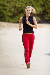 Lächelnde Frau beim Joggen am Strand in voller Länge - CAVF21993
