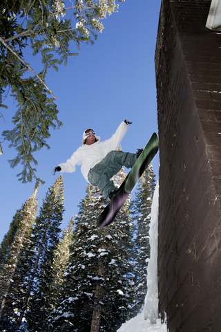 Mann beim Snowboarden an der Wand gegen Bäume, lizenzfreies Stockfoto