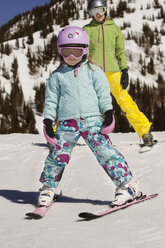 Mädchen und Mutter in voller Länge mit Skiern auf einem verschneiten Berg stehend - CAVF22009