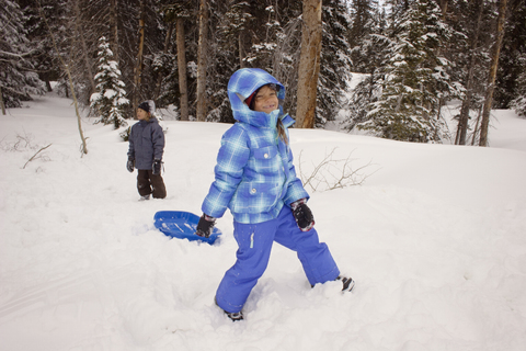 Glückliche Geschwister spielen auf einem schneebedeckten Feld vor Bäumen, lizenzfreies Stockfoto