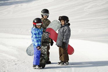 Geschwister tragen Snowboards, während sie auf einem verschneiten Feld stehen - CAVF22016