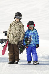 Lächelnde Geschwister, die Snowboards tragen, während sie auf einem schneebedeckten Feld stehen - CAVF22018