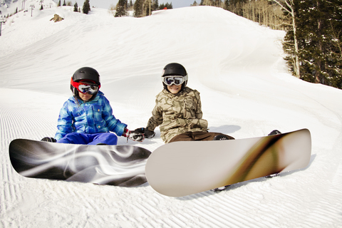 Geschwister mit Snowboards auf einer verschneiten Wiese sitzend, lizenzfreies Stockfoto