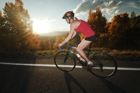 Radfahrerin auf der Straße bei Sonnenuntergang, lizenzfreies Stockfoto