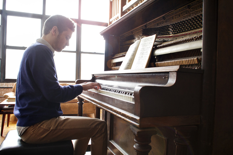 Seitenansicht eines Mannes, der zu Hause am Fenster Klavier spielt, lizenzfreies Stockfoto