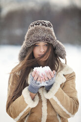 Porträt einer schönen Frau, die warme Kleidung trägt und Schnee hält - CAVF22080