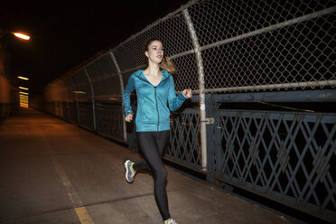 Junge Frau joggt nachts auf einer Brücke - CAVF22108