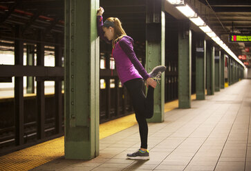 Side view of young woman stretching while leaning on column at railroad station - CAVF22124