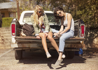 Glückliche Freundinnen sitzen auf dem Kofferraum eines Fahrzeugs an einem sonnigen Tag - CAVF22126