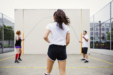 Woman walking towards friends holding jump ropes on street against wall - CAVF22145