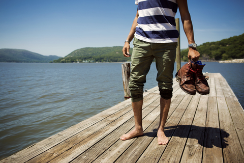 Tiefschnitt eines Mannes mit Schuhen, der auf einem Steg über einem See steht, lizenzfreies Stockfoto