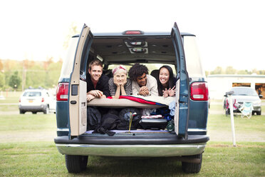 Friends lying in back of camping van on grassy field - CAVF22225