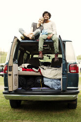 Smiling couple sitting on hood of camping van against clear sky - CAVF22229