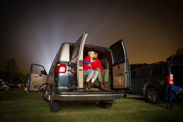 Couple wrapped in blanket sitting at back of car during drive-in movie - CAVF22231