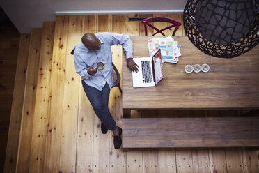 Overhead view of senior man using laptop while having coffee at home - CAVF22237