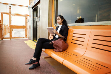 Nachdenkliche Frau, die ein digitales Tablet benutzt, während sie auf einer orangefarbenen Bank in der Stadt sitzt - CAVF22248