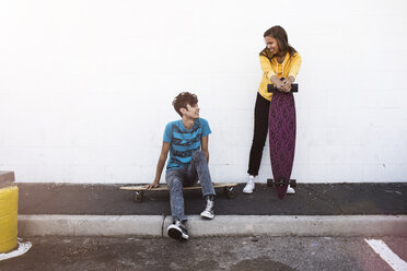 Friends relaxing with skateboards on sidewalk against white wall - CAVF22260