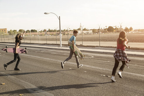 Freunde mit Skateboards laufen auf der Straße gegen den klaren Himmel - CAVF22263