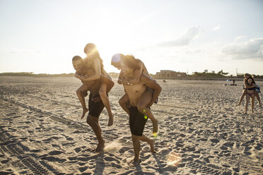Freunde genießen Huckepackfahrten am Strand gegen den Himmel an einem sonnigen Tag - CAVF22315