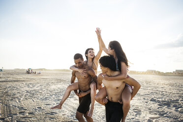 Weibliche Freunde geben High Five, während sie am Strand Huckepack reiten - CAVF22317