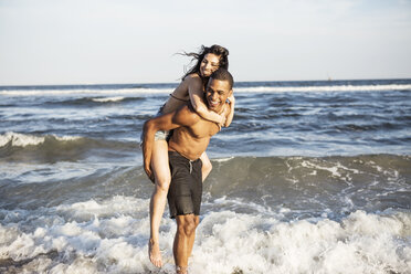 Couple enjoying piggyback ride at shore against sea - CAVF22318