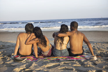 Rückansicht von Paaren am Strand sitzend an einem sonnigen Tag - CAVF22322