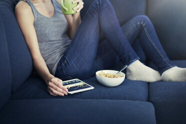 Midsection of woman using digital tablet while eating breakfast on sofa - CAVF22332