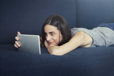 Lächelnde Frau auf dem Sofa liegend und mit digitalem Tablet zu Hause - CAVF22334