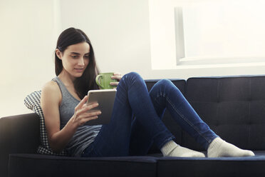 Frau sitzt auf dem Sofa und benutzt ein digitales Tablet - CAVF22337