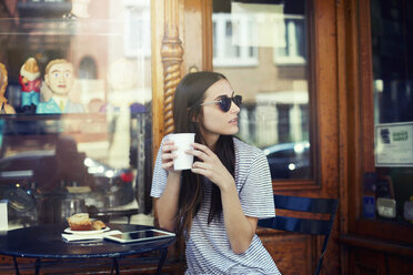 Schöne Frau hält Kaffee und sitzt in einem Straßencafé - CAVF22342