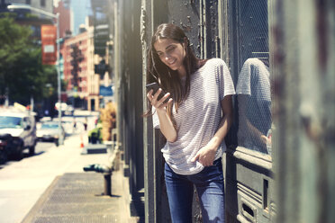Lächelnde Frau mit Smartphone an einem sonnigen Tag - CAVF22346