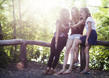 Happy sisters taking selfie while resting on railing at park - CAVF22385