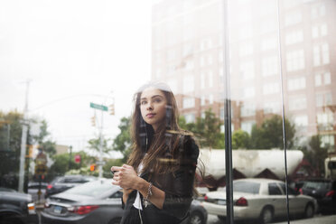 Confident woman standing against cars seen through glass window - CAVF22386